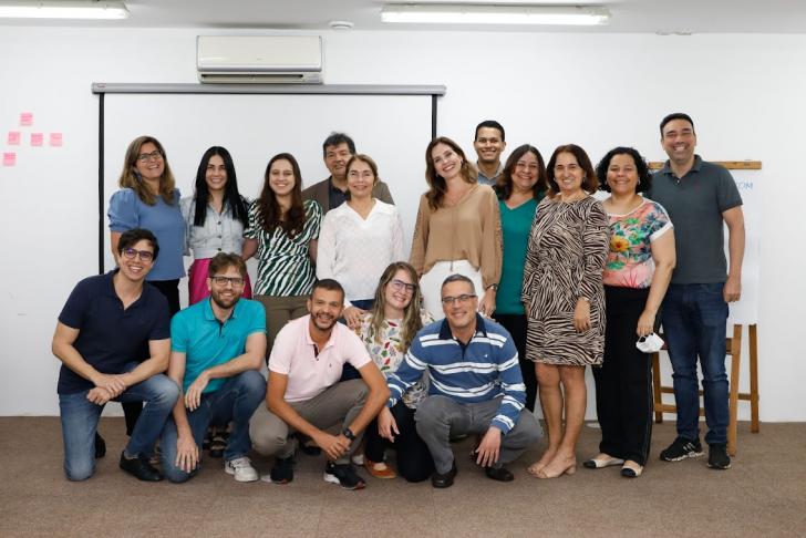 Onze pessoas lado a lado, em pé, em uma sala de aula. À frente, mais cinco pessoas agachadas.
