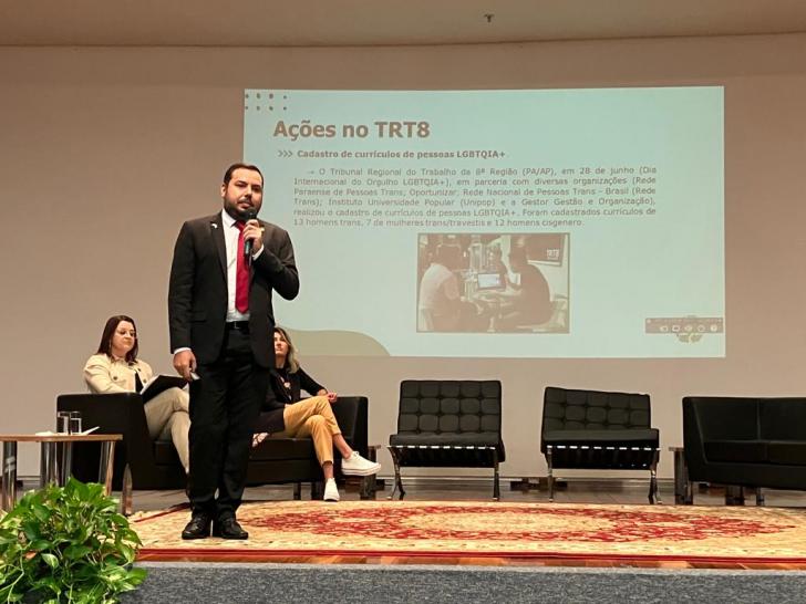 Homem em pé com terno preto, blusa branca e gravata vermelha.