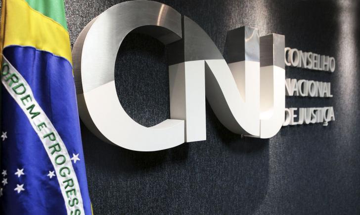 Fotografia do logo do Conselho Nacional de Justiça ao lado de uma bandeira do Brasil.