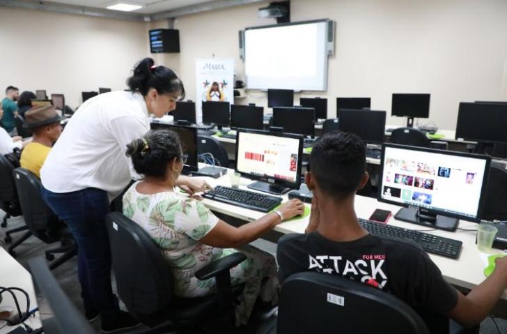 Fotografia em ambiente fechado de uma sala de aula repleta de computadores.