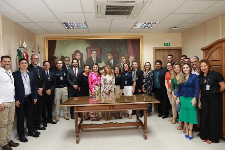 #ParaTodosVerem: Fotografia em ambiente interno, com dezenas de pessoas reunidas em pé sorrindo para a foto. Fim da descrição.