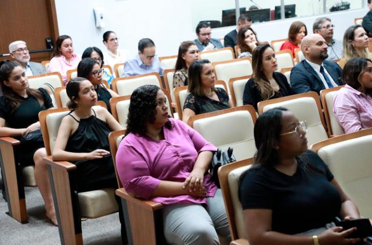 ParaTodosVerem: Fotografia de um auditório com diversas pessoas entre homens e mulheres. Fotografia de um homem branco portando