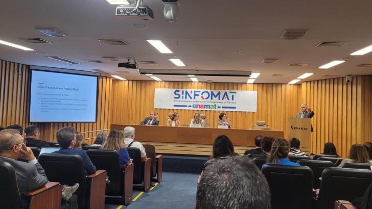 Foto colorida em um ambiente fechado, palestra sobre o uso do Chat-JT no ensino e trabalho diário, com painel de debatedores e p