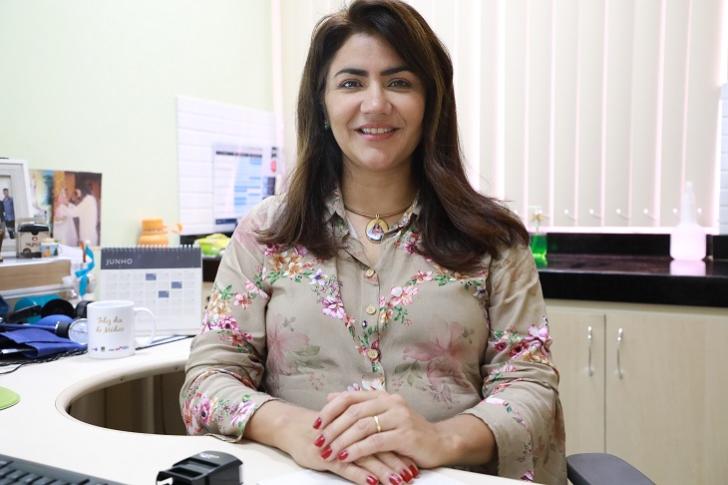 #ParaTodosVerem: Fotografia coloria em ambiente fechado, centralizada na imagem a médica Luciana Ramoa, posando para a foto e so