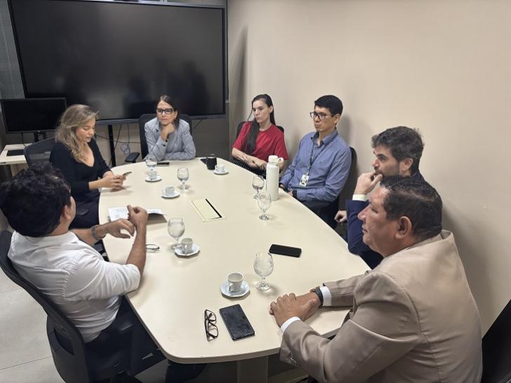 #ParaTodosVerem: Fotografia colorida em ambiente fechado. A foto mostra homens e mulheres sentados em reunião