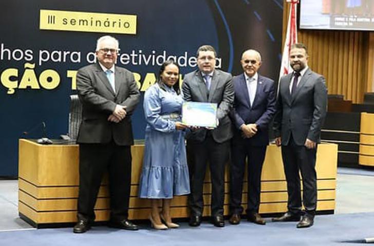 #ParaTodosVerem: Fotografia colorida. Na imagem, estão cinco pessoas de pé, uma mulher e quatro homens, todos sorriem para a fot