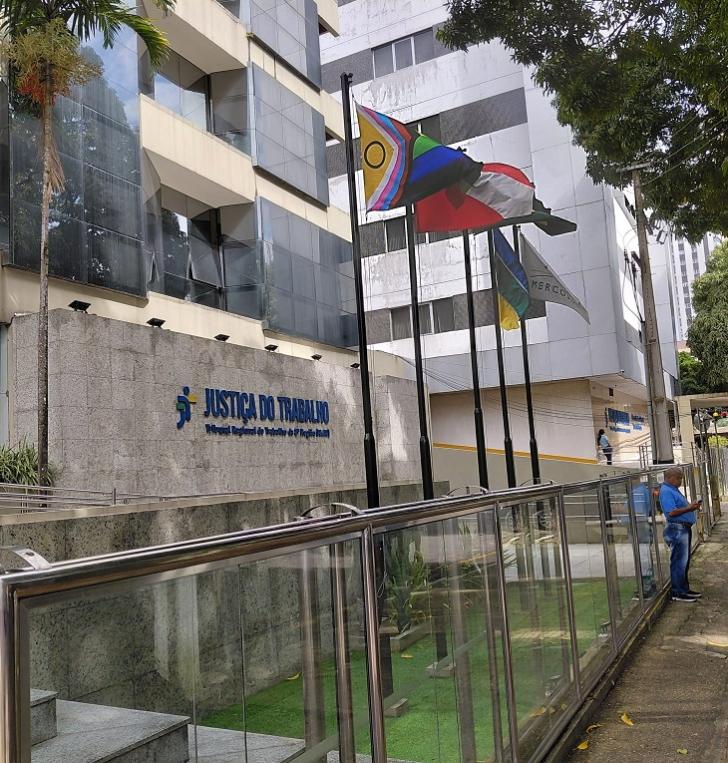 Foto colorida em ambiente aberto mostrando a fachada do TRT8 e as bandeiras do orgulho LGBTQIAPN+, do Mercosul, Brasil, do Pará 