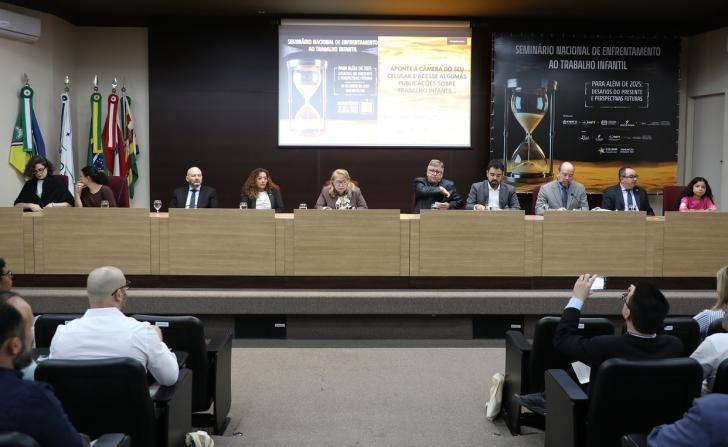 Foto dos participantes da mesa da abertura posicionados para o início da mesa. Mais a frente, o público sentado também aguarda.
