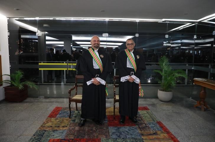 Fotografia em ambiente fechado de dois homens, lado a lado, vestido com uma toga