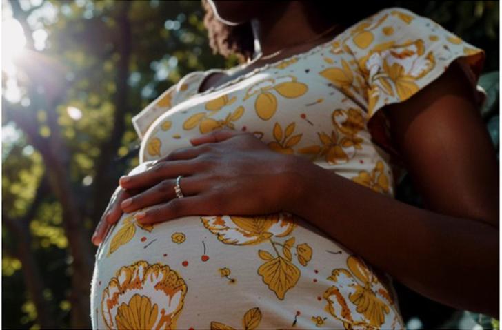 Mulher gestante com vestido florido branco e amarelo, com a mão acima da barriga