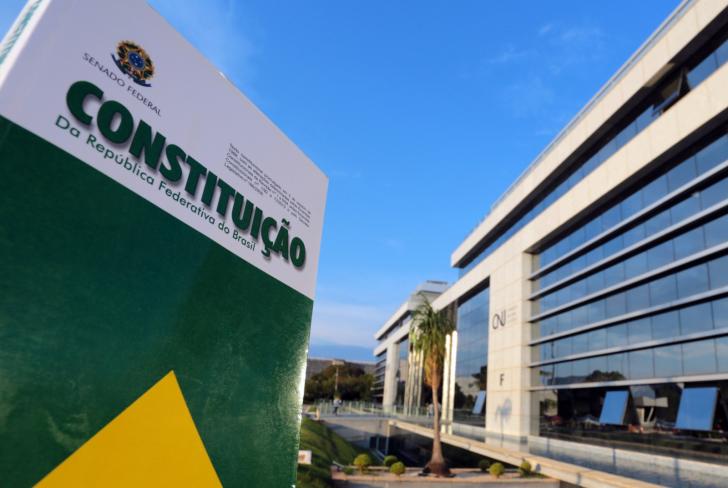 Foto colorida que mostra a Constituição da República Federativa do Brasildo em frente a fachada no CNJ. 