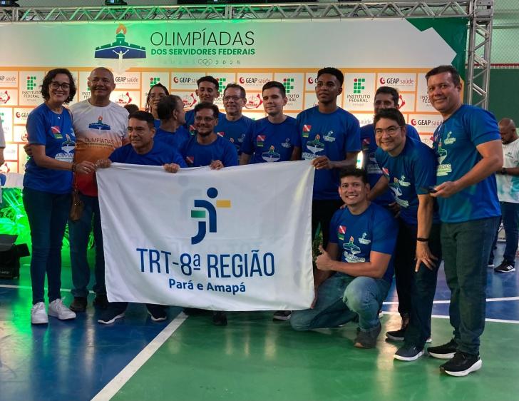 #ParaTodosVerem: Fotografia colorida reunindo homens e mulheres, todos estão em pé sorrindo para a foto e segurando a bandeira d