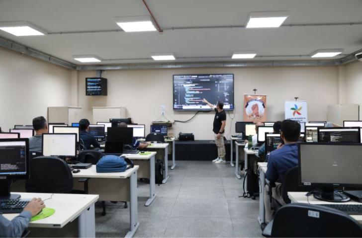 ParatodosVerem: Fotografia de um laboratório de informática, com diversas pessoas sentadas mexendo nos computadores. No centro,
