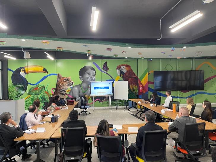 #ParaTodosVerem: Foto em espaço fechado com algumas pessoas sentadas em frente a uma tela, entre homens e mulheres.