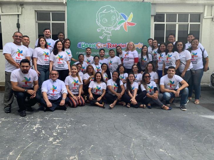 Padrinhos , voluntários e servidores reunidos enfrente ao backdrop do Combate ao Trabalho Infantil