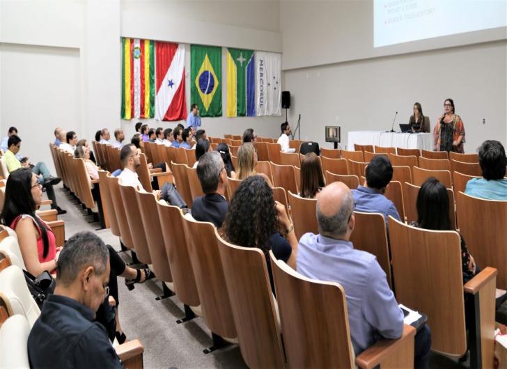 Na foto: O auditório cheio de pessoas com a palestrante ao fundo.