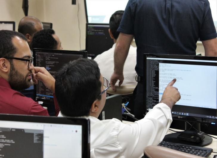 Na foto: dois servidores da SETIN participando da capacitação, conversando sentados de frente para computadores.