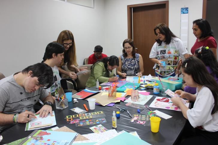 Servidores do CEJUSC e jovens com síndrome de down ao redor de uma mesa fazendo atividades de colagens