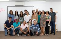 Onze pessoas lado a lado, em pé, em uma sala de aula. À frente, mais cinco pessoas agachadas. 