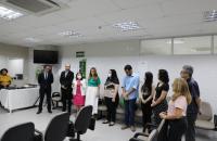 Dez pessoas lado a lado em uma sala com paredes brancas e cadeiras espalhadas