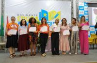 Fotografia em ambiente fechado com 8 mulheres exibindo certificados
