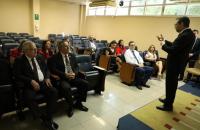 Fotografia em ambiente fechado que reúne pessoas durante apresentação de um painel de trabalho