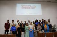Fotografia em ambiente fechado de diversas pessoas em pé, lado a lado, formando uma fila mais acima e outra mais abaixo.