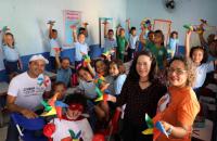 #ParaTodosVerem: Foto em ambiente fechado, sala de aula repleta de alunos sorridentes, segurando um catavento colorido.