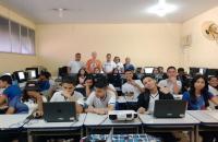 Ambiente de sala de informática com vários computadores e os alunos são crianças e adolescentes.