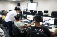 Fotografia em ambiente fechado de uma sala de aula repleta de computadores.