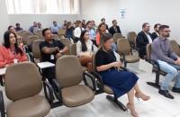 Fotografia em ambiente fechado de dezenas de pessoas sentadas lado a lado.