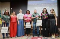 Fotografia em ambiente fechado que reúne sete pessoas em pé, lado a lado, entre homens e mulheres.