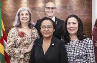 Fotografia em amFotografia em ambiente fechado que reúne três mulheres, sendo uma negra e duas brancas lado a lado. Atrás