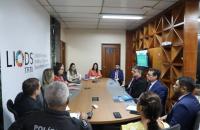 #ParaTodosVerem: Fotografia em ambiente fechado, composta por treze pessoas sentadas, lado a lado,em uma mesa de reunião.