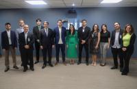 Fotografia em ambiente fechado com 12 pessoas em pé, lado a lado, sorrindo, sendo 4 mulheres e 8 homens