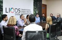 Fotografia de um grupo de servidores e dois magistrados conversando, sentados em uma mesa oval no Laboratório de Inovação do TRT