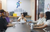 Fotografia em ambiente fechado que reúne quatro mulheres e um homem, sentados em volta de uma mesa.