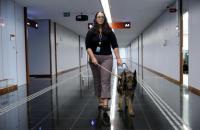 Fotografia em um ambiente fechado, no centro uma mulher caminhando com seu cão guia.