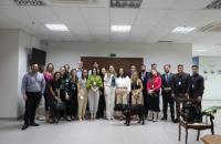 Fotografia em ambiente fechado. No centro, estão homens e mulheres de pé e sorrindo para a foto. Ao lado da palestrante Maria Vi