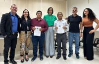 Fotografia em ambiente fechado com sete pessoas, entre homens e mulheres, todos estão de pé e sorrindo para a foto. 