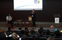 Adriana Silva e Rodrigo Calixto, representando o Sesc Pará, no palco do auditório do TRT-8. Ela está de pé e fala ao microfone. 