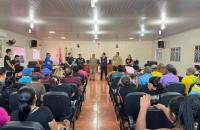 #ParaTodosVerem: Fotografia colorida em ambiente fechado, contendo diversas pessoas sentadas e 9 pessoas em pé.