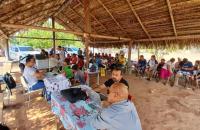 Fotografia colorida em ambiente aberto na aldeia Yetá, na foto contém pessoas sentadas esperando atendimento e outros sendo aten