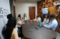 Fotografia em ambiente fechado que reúne homens e mulheres e ao fundo a tela com participantes online 