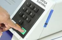 Foto com detalhe de mão apertando o botão "confirma" da urna eletrônica de votação brasileira. 