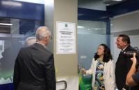 Fotografia em ambiente fechado que reúne uma mulher branca e dois homens descerrando a placa de inauguração