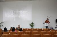  Fotografia colorida do auditório da EJUD, na foto está 6 pessoas sentadas assistindo a palestra e o palestrante Dr. Eric Alvare