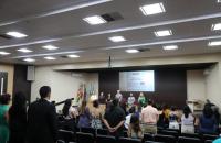 Foto da cerimônia de formatura, com magistrados, convidados e formandas de pé no momento do hino nacional.