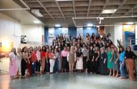 Fotografia em ambiente externo que reúne dezenas de mulheres lado a lado, em pé e sorrindo