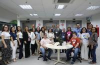 Foto colorida em ambiente fechado os presentes estão sorrindo, com alguns homens de terno e outros com roupa casual e mulheres c